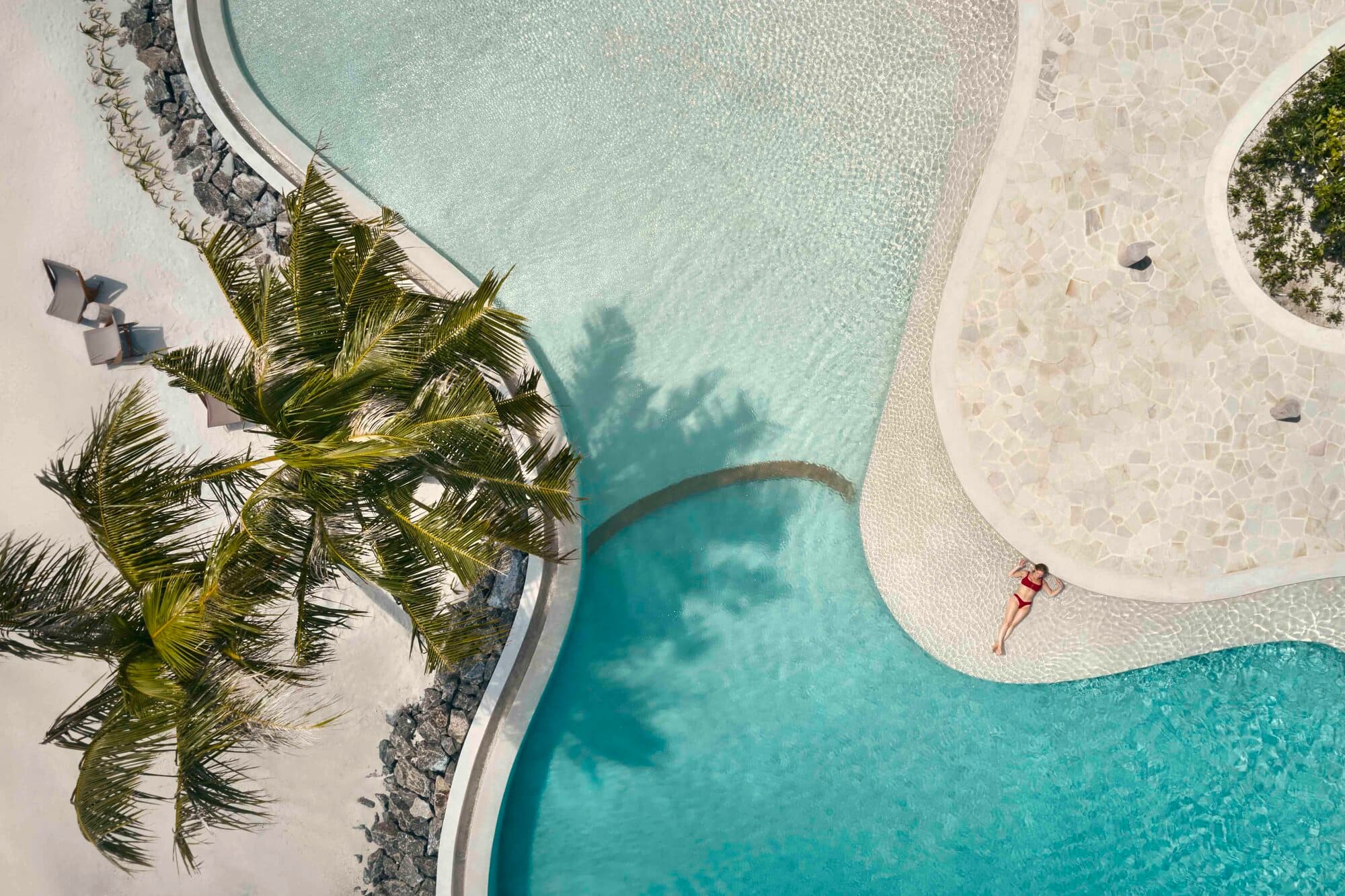 Die geschwungenen Kurven des Fari Beach Club Pools von oben, eine einzelne Frau im Türkis