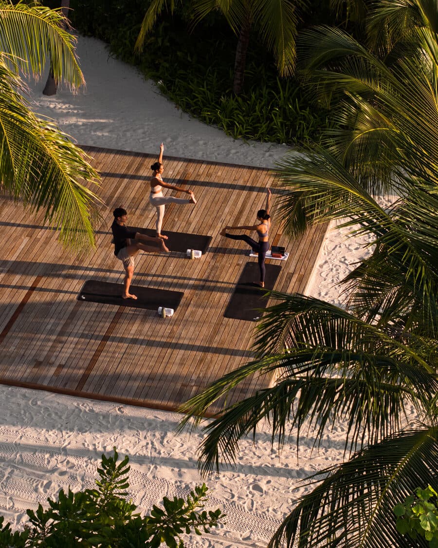 Yoga bei Sonnenaufgang auf dem Holzdeck am Strand